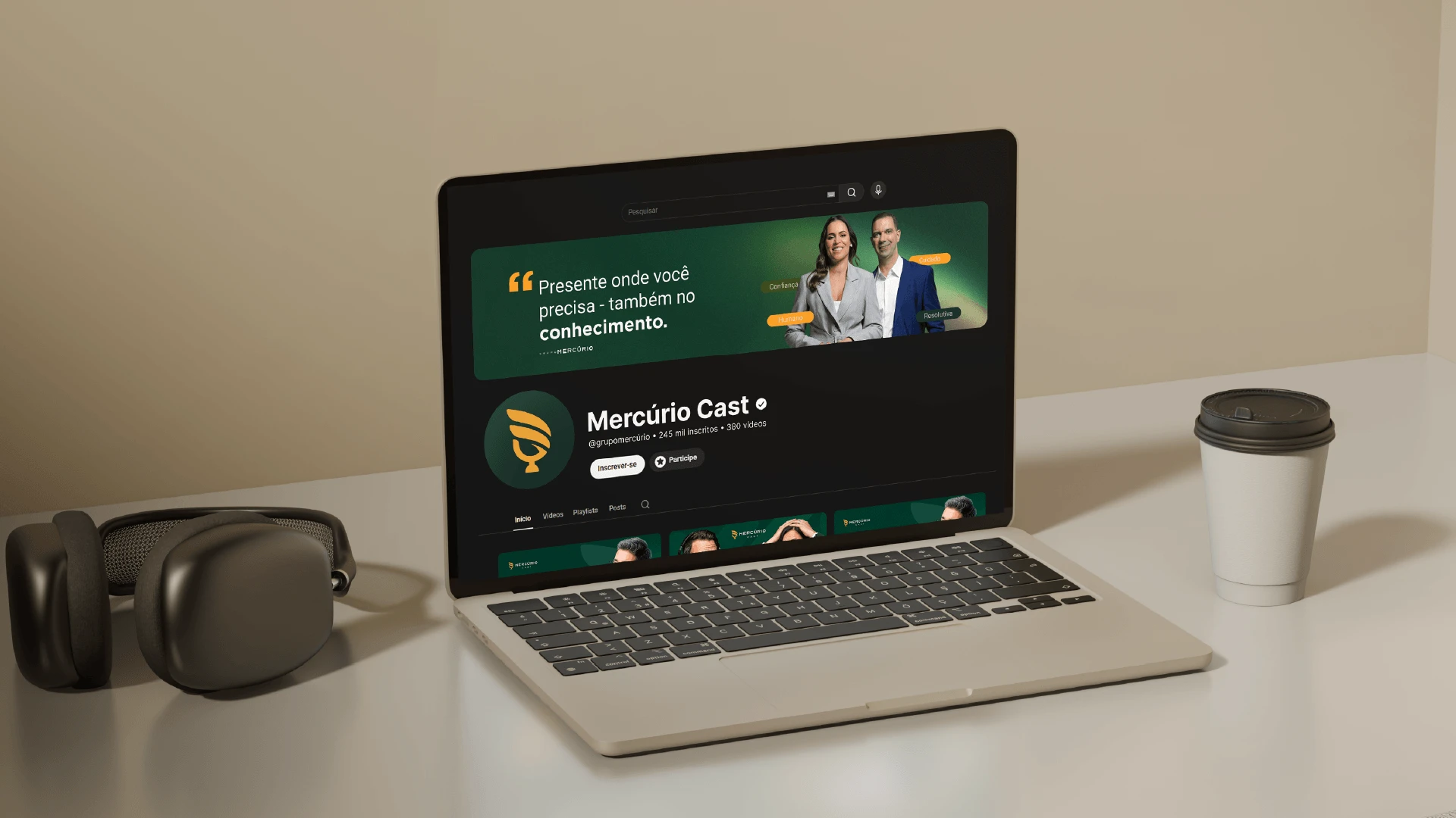 Página do canal Mercúrio Cast no YouTube aberta em um notebook, ao lado de um fone de ouvido e um copo de café