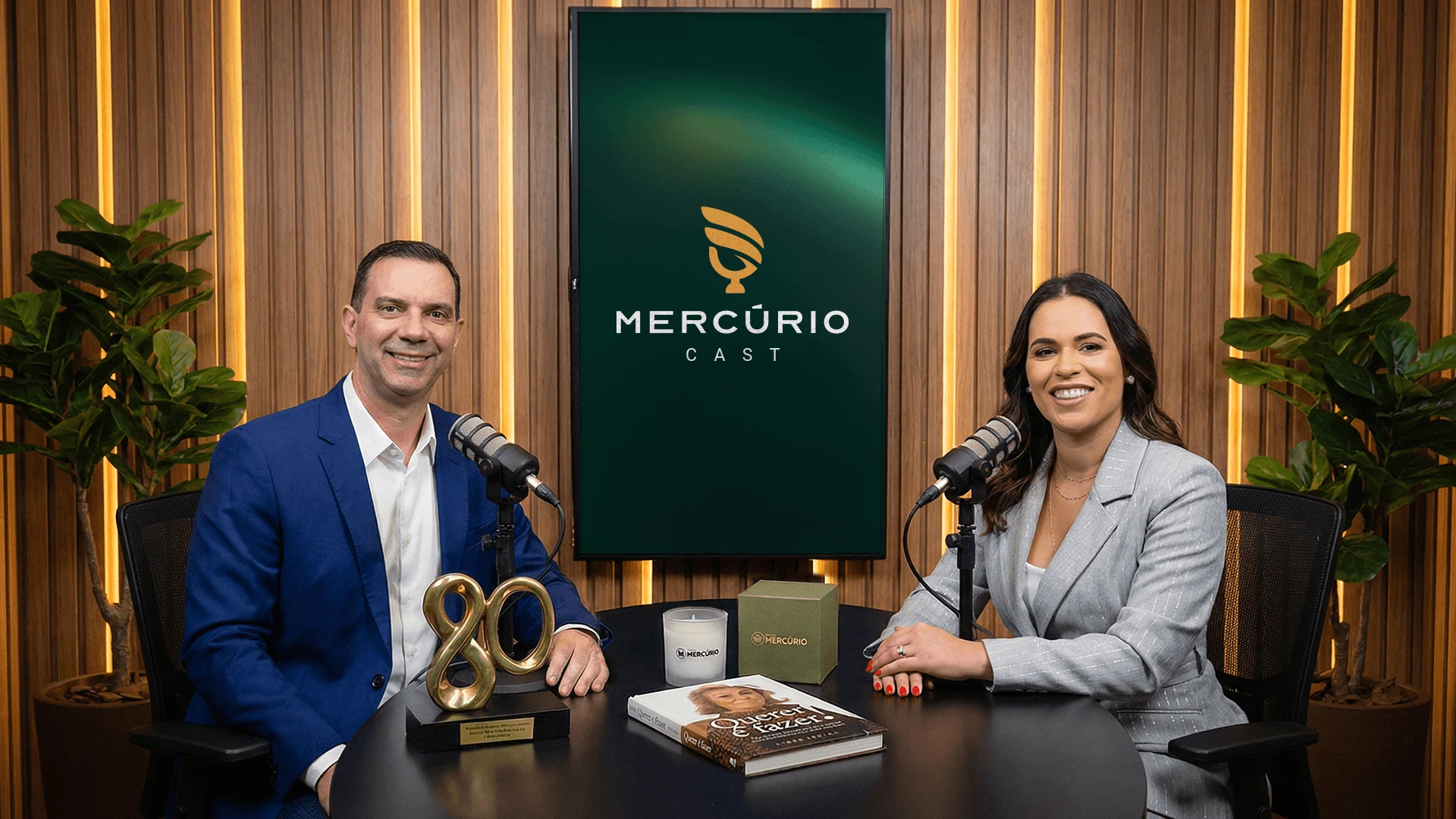 Apresentadores do Mercúrio Cast no estúdio, com o logo do podcast na tela ao fundo
