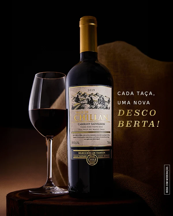 Post "Cada taça, uma nova descoberta!": garrafa de Valle de Chillán Cabernet Sauvignon ao lado de uma taça, sobre tronco de madeira