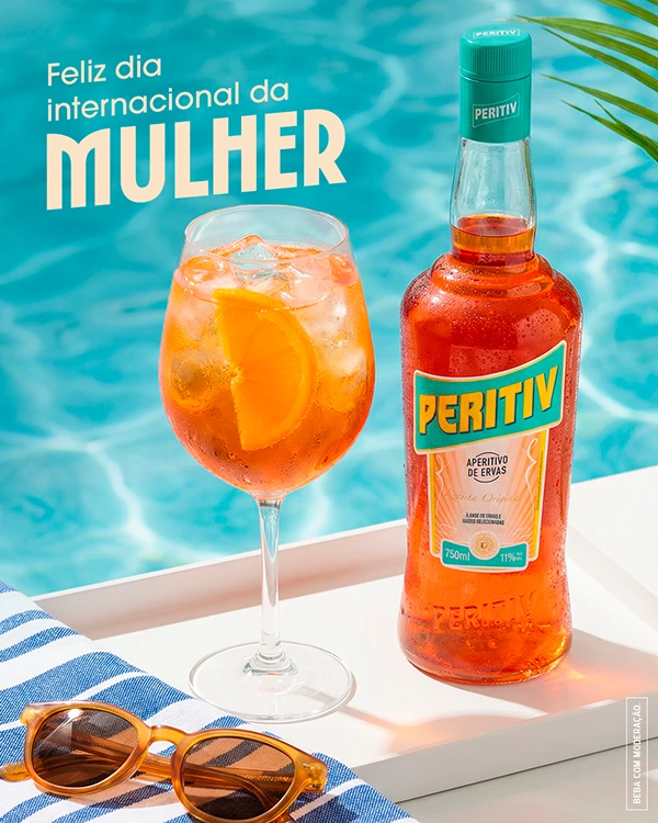 Post "Feliz Dia Internacional da Mulher": taça de drink e garrafa de Peritiv à beira da piscina, com óculos de sol sobre uma toalha listrada