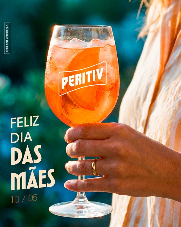 Post "Feliz Dia das Mães, 10/05": mão segurando uma taça de drink de Peritiv com laranja
